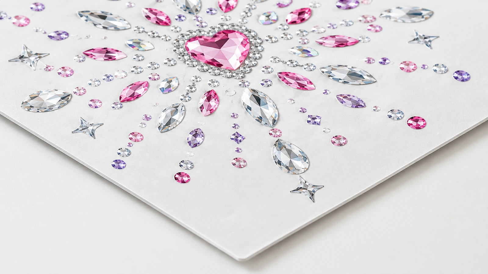 Cận cảnh họa tiết rhinestone tâm hình trái tim màu hồng, với đá trong suốt, hồng và tím trên tờ giấy trắng